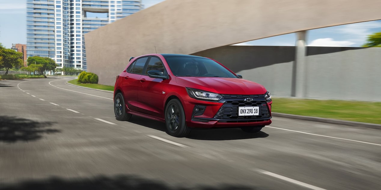 Vista frontal lateral del Onix 2026 color Rojo Jinx conduciendo en ruta urbana