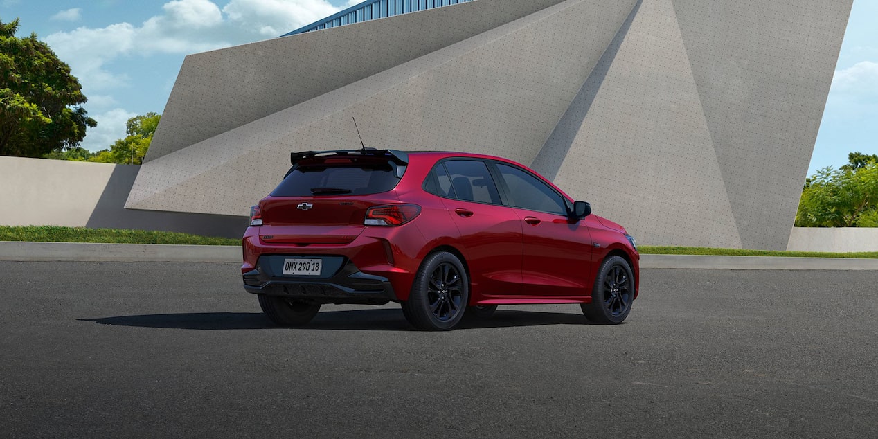 Vista trasera lateral del Onix 2026 color Rojo Jinx estacionado en área urbana